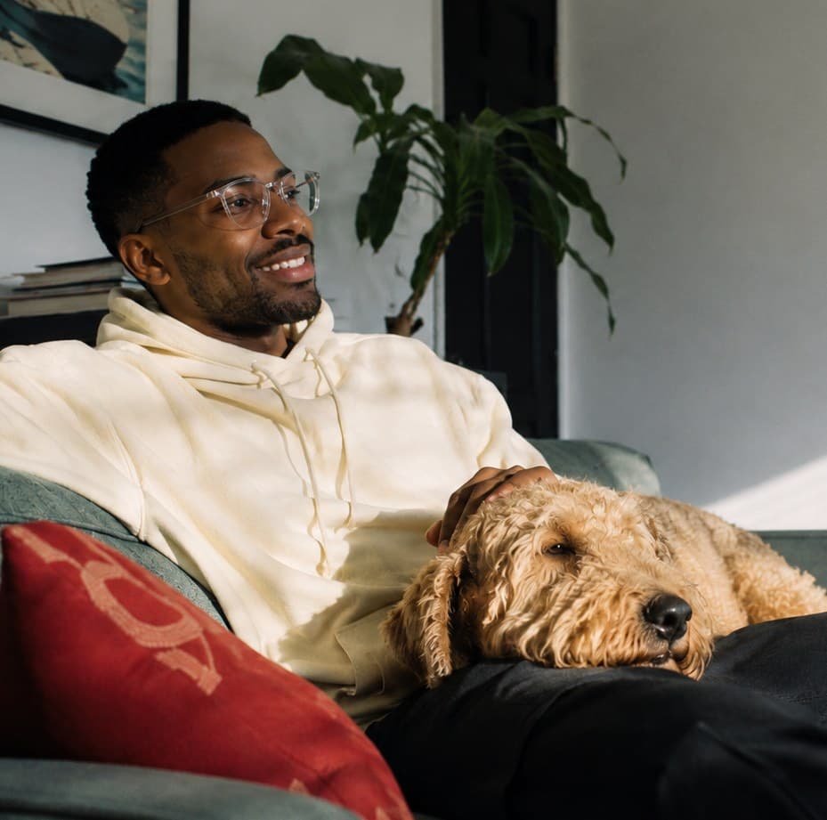A man relaxing on a couch with his dog resting beside him