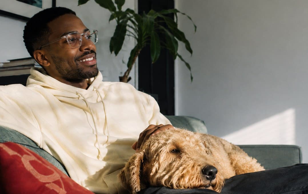 A man relaxing on a couch with his dog resting beside him